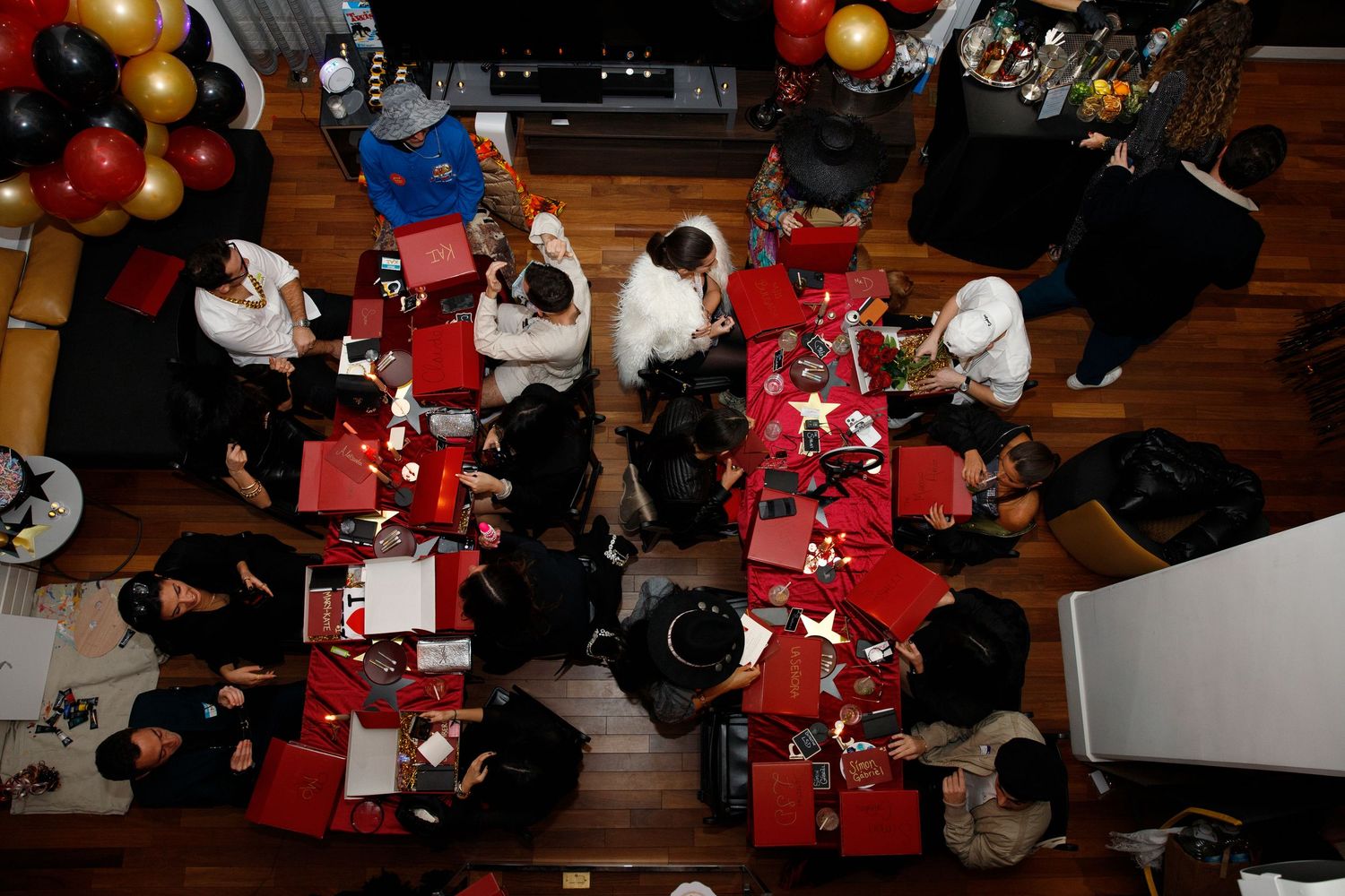 Aerial view of dinner party guests seated at red-clothed tables with festive balloon decorations.