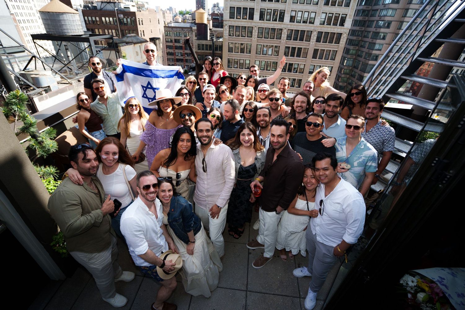 Large group of people gathered on a rooftop terrace for a social event in the city.