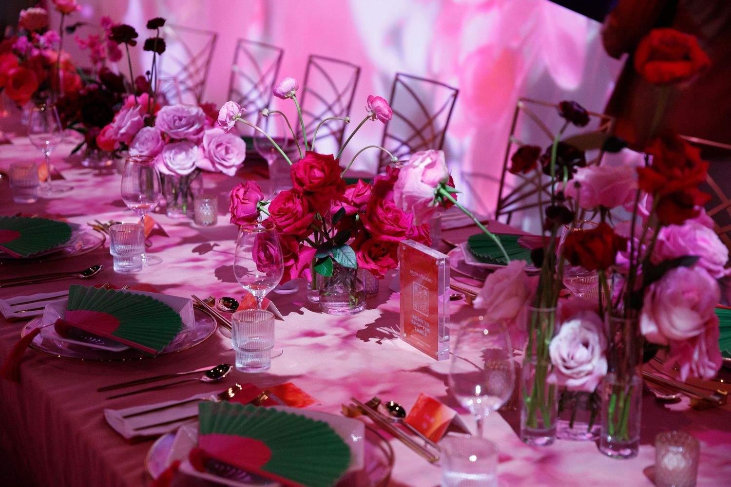 Elegant table setting with pink roses and glassware under romantic pink lighting at an upscale event.
