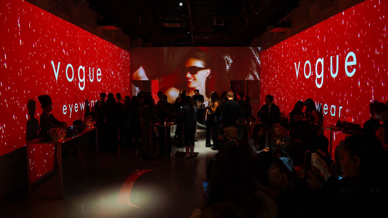 Vogue event space with red illuminated walls and scattered crowd silhouettes.