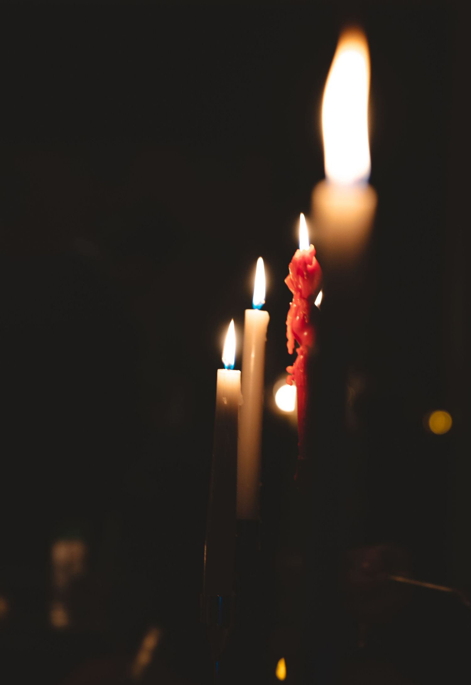 Lit white candles and red wax against a dark background create a moody atmosphere.