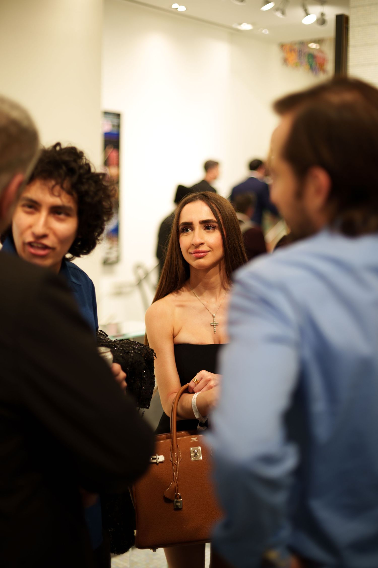 Guests mingling at upscale gallery event with white walls and track lighting.