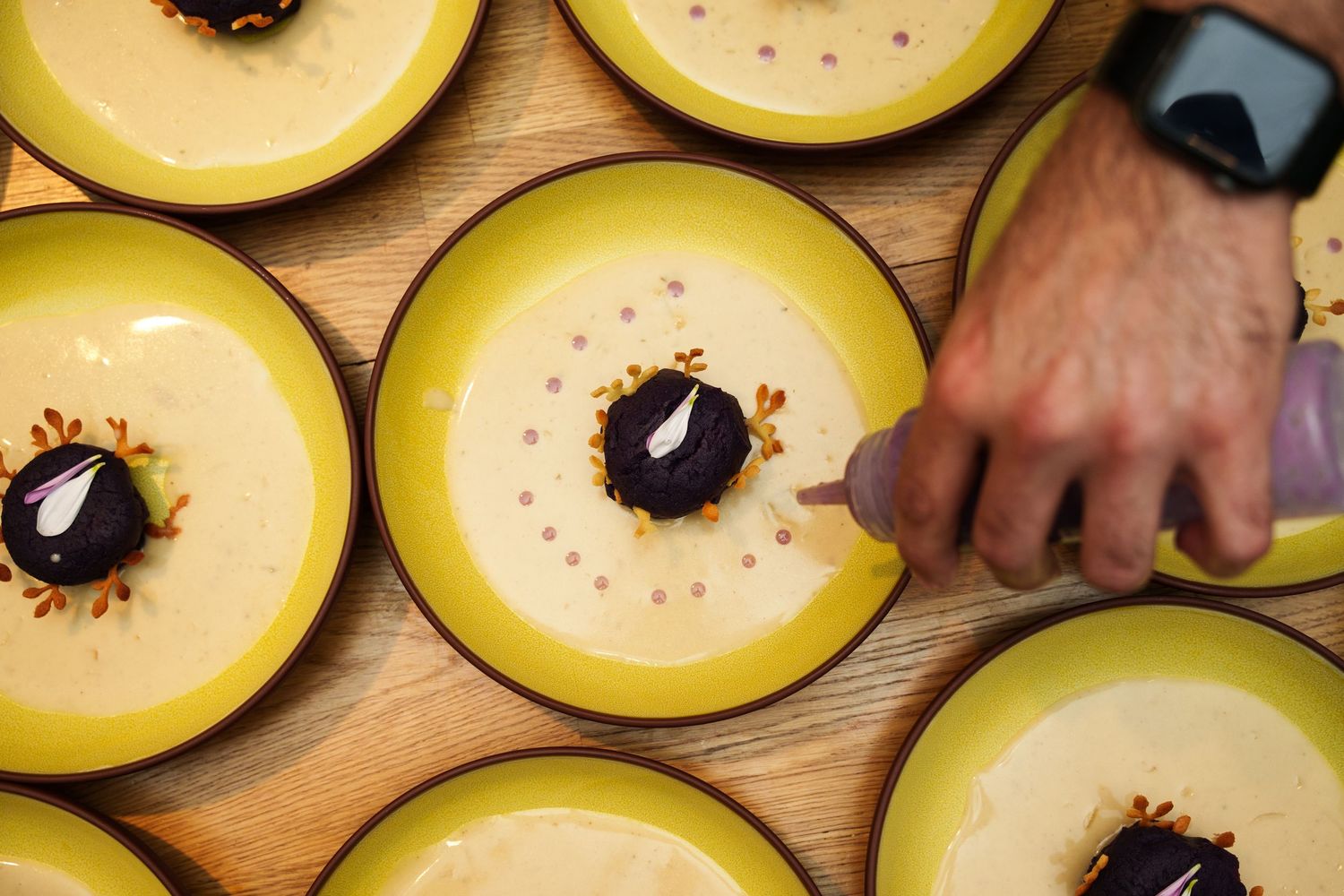 Overhead shot of yellow bowls filled with creamy soup arranged in rows on a wooden table.
