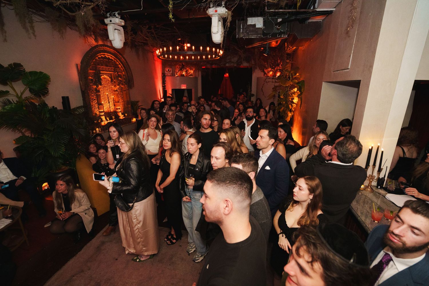 Crowded party venue with string lights and guests mingling in formal attire.