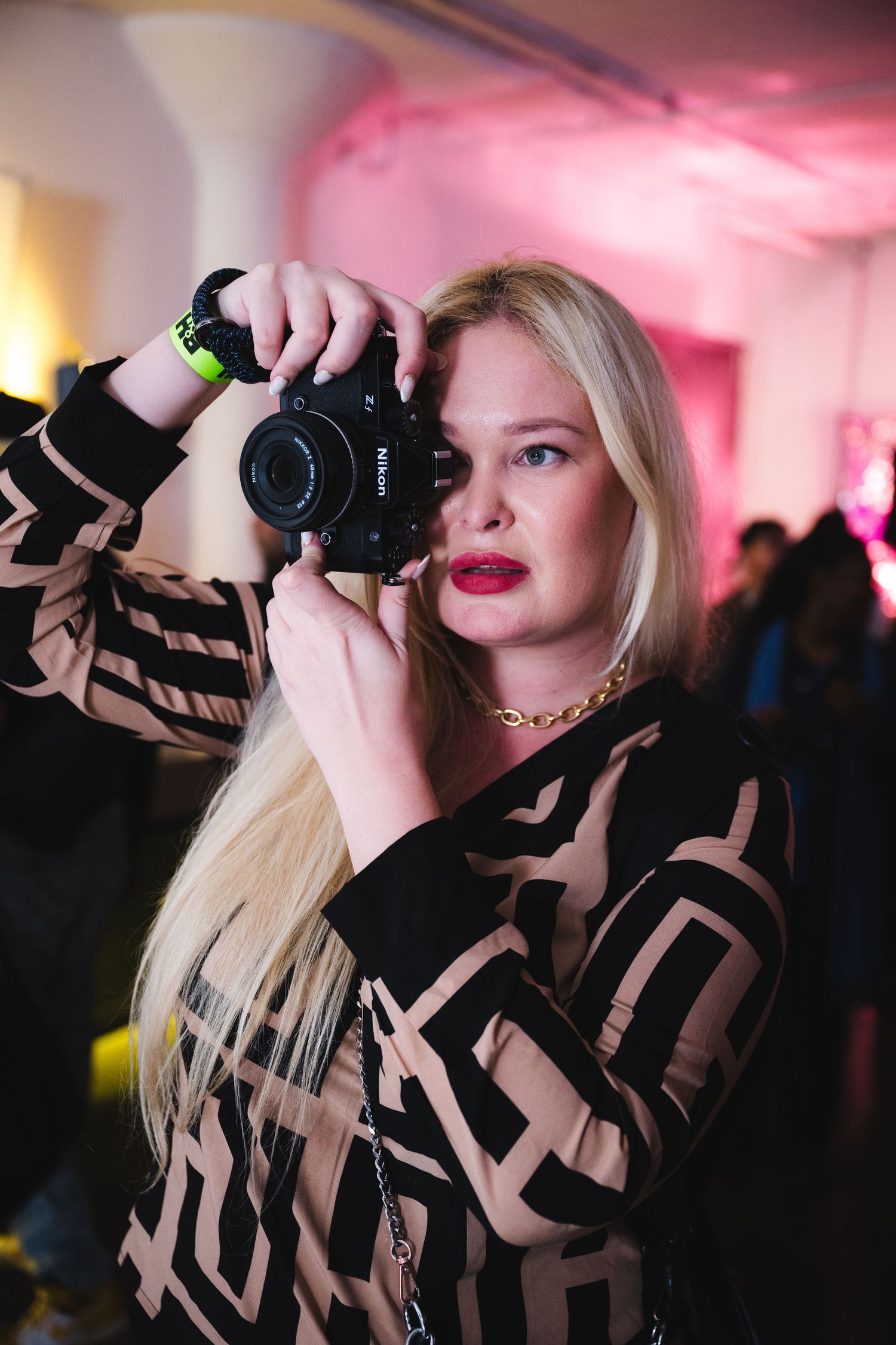 A photographer wearing black captures photos at an event with pink ambient lighting.