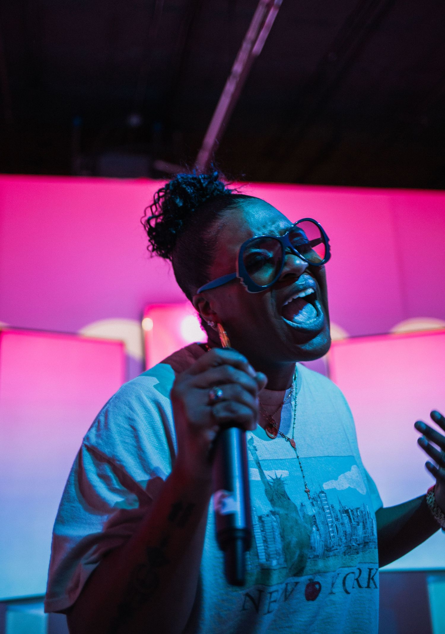Performer sings passionately into microphone under dramatic pink and blue lighting.