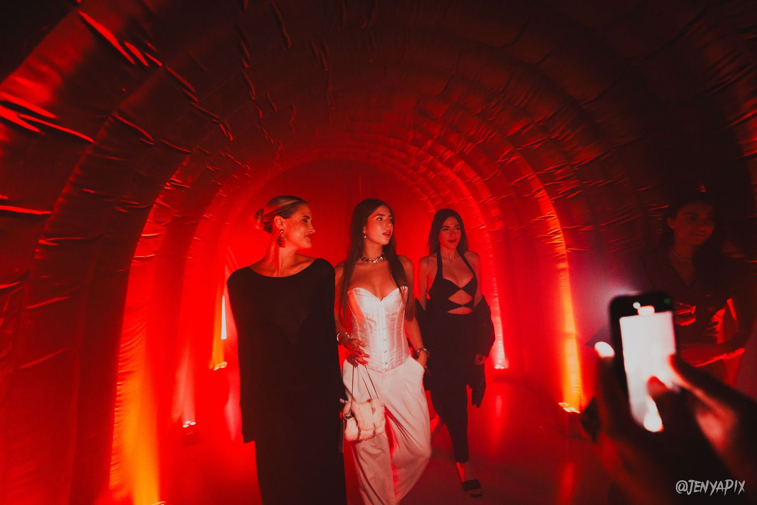 People walking through a red-lit tunnel archway at an event venue.