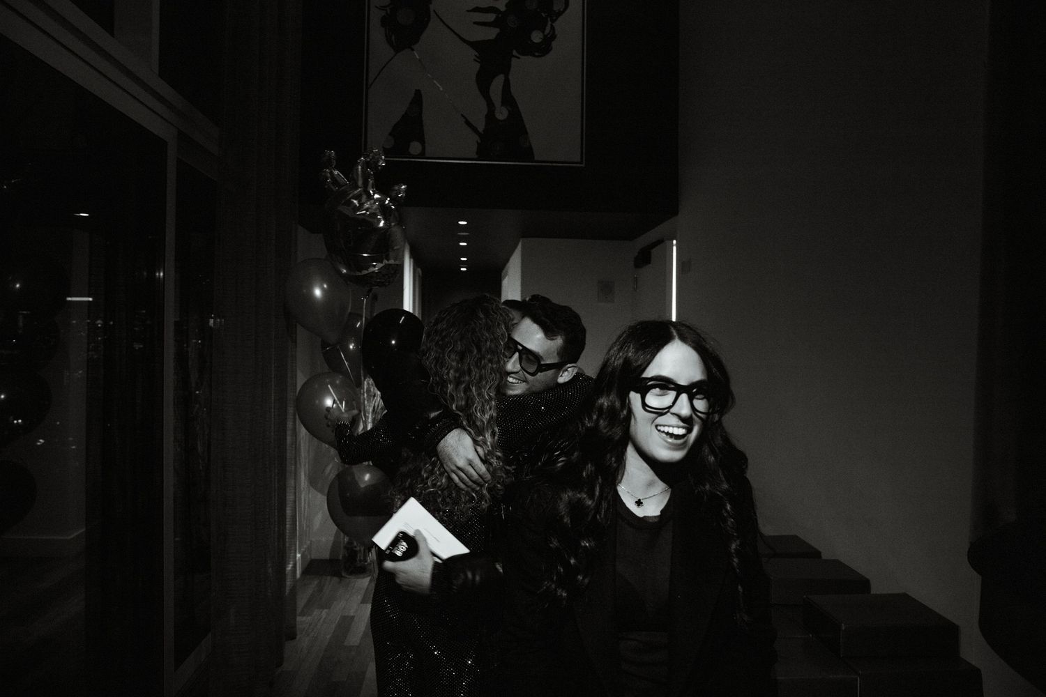 Partygoer in dark attire and glasses poses at a dimly lit event.