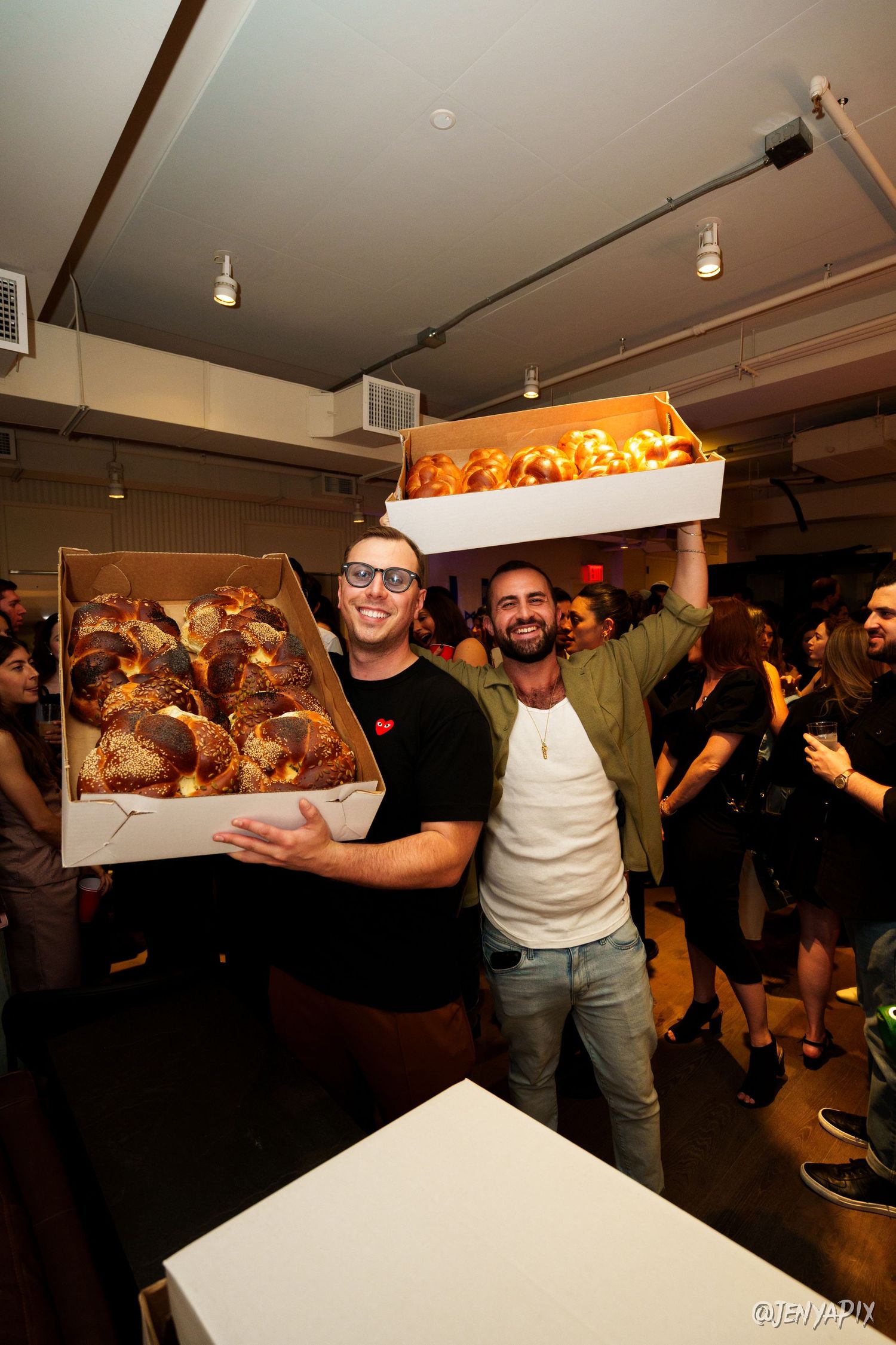 Two people holding boxes of fresh baked goods at a crowded party.