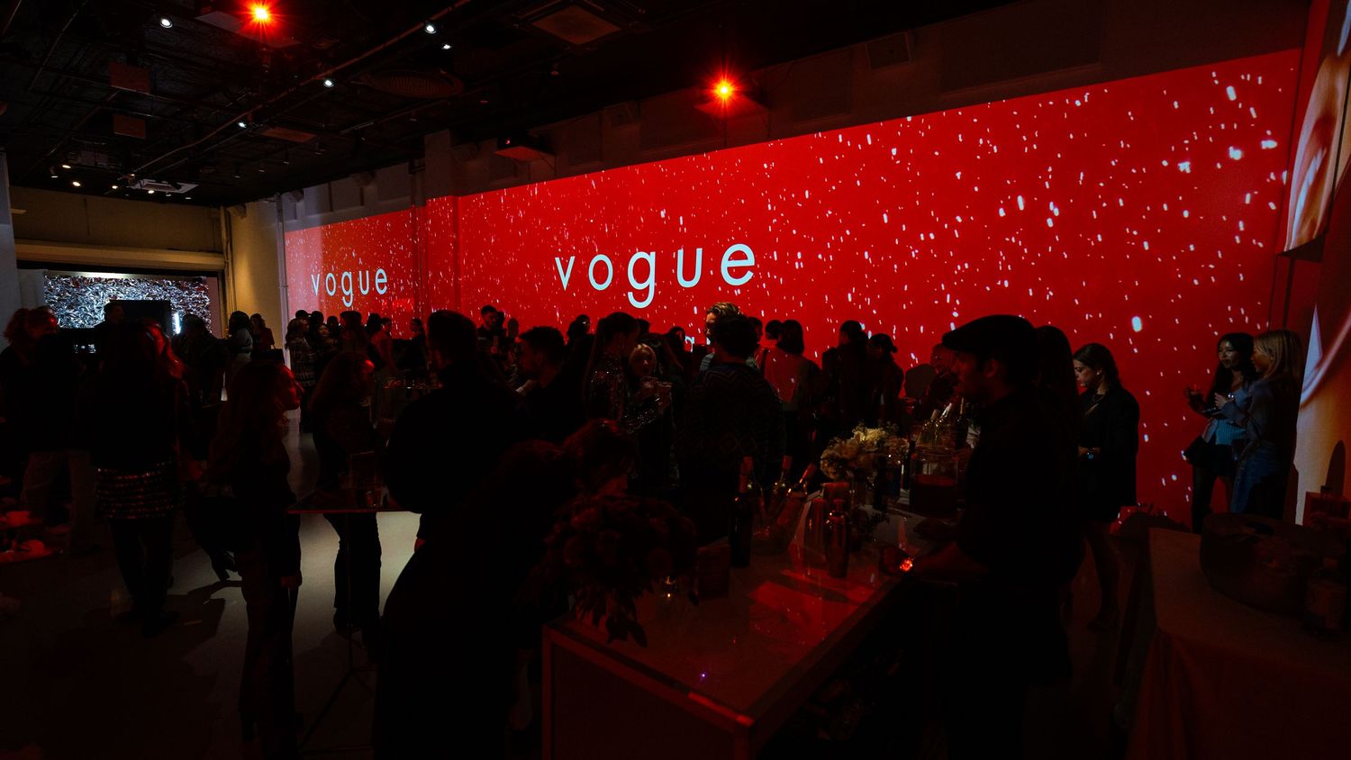 Crowded event space with red illuminated Vogue branding on walls.