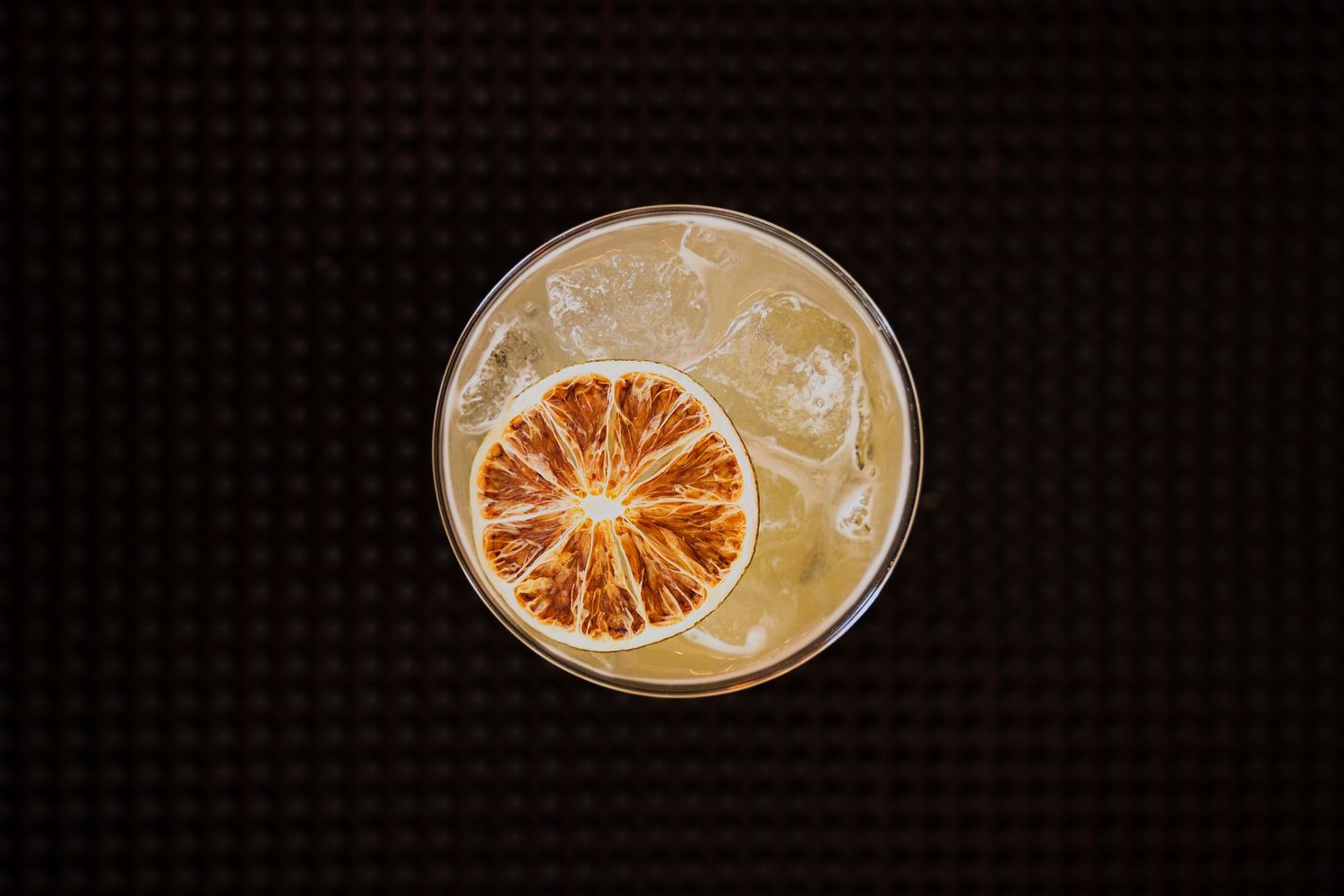 Overhead view of a craft cocktail garnished with a dried orange slice.