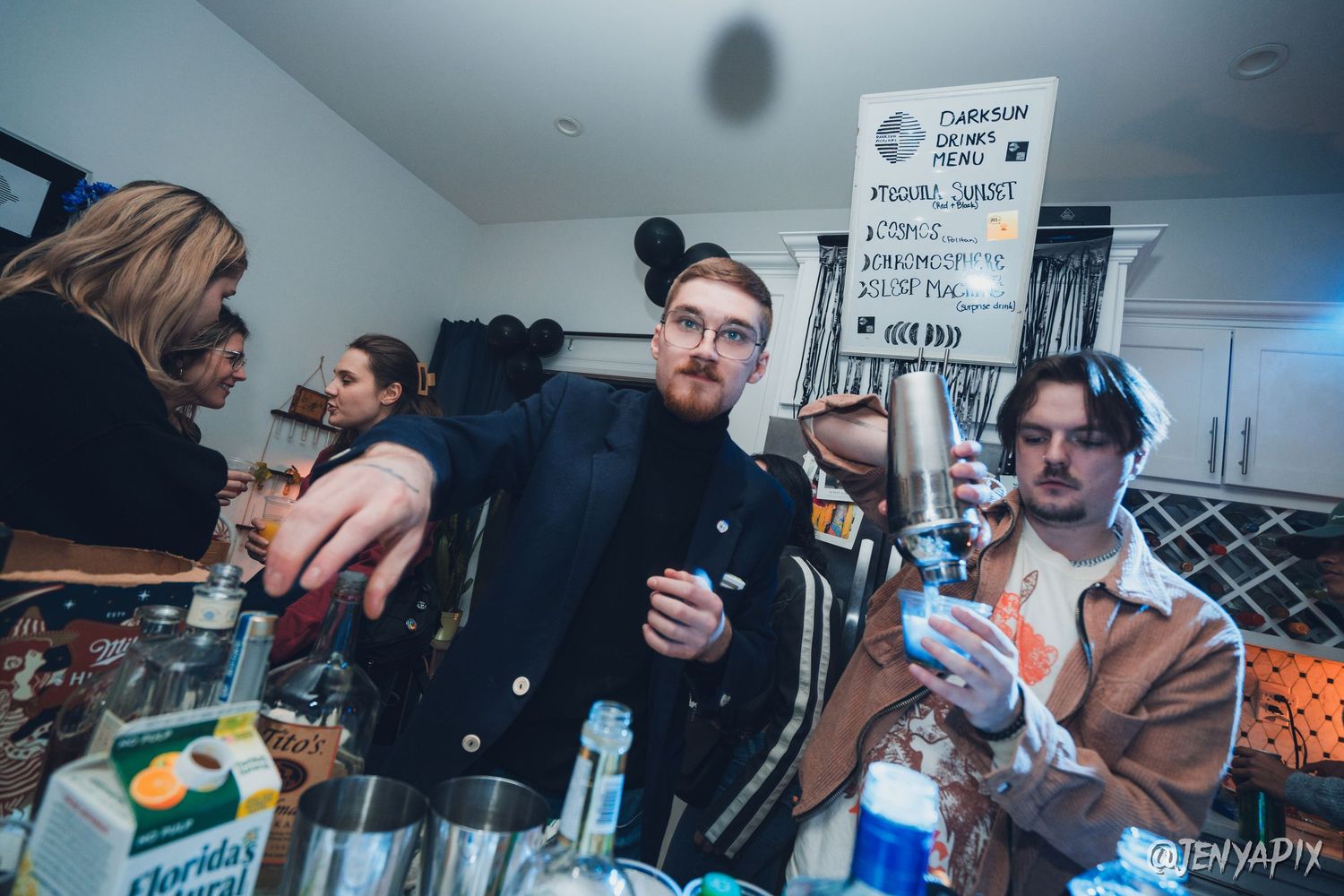 Group hanging out at a party with drinks and a handwritten sign on the wall.