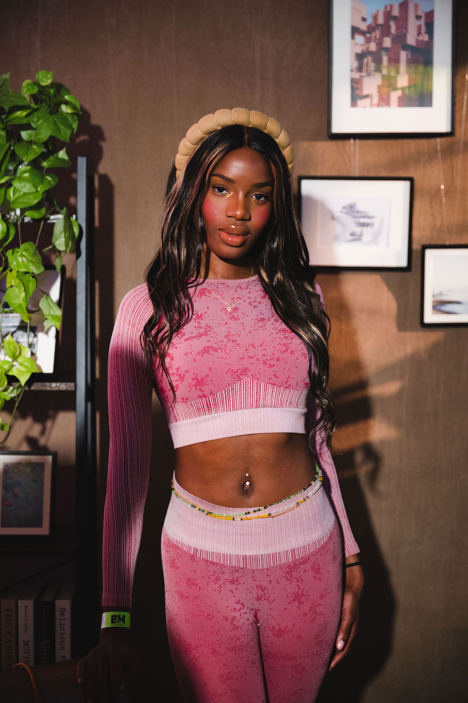 Person in pink athletic wear posing against wall with artwork and plants.