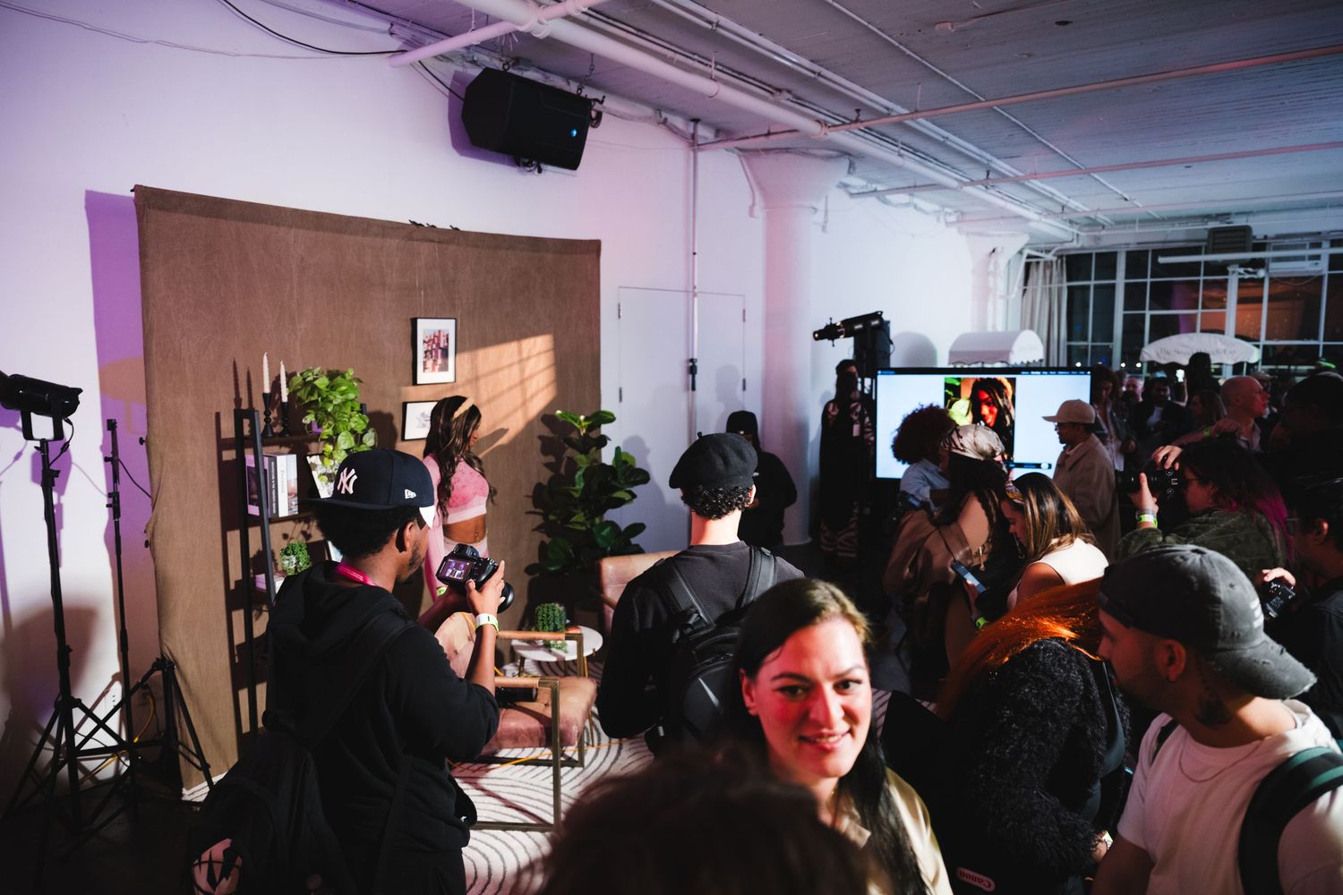 A crowded photo shoot event with photographers and attendees under purple lighting.