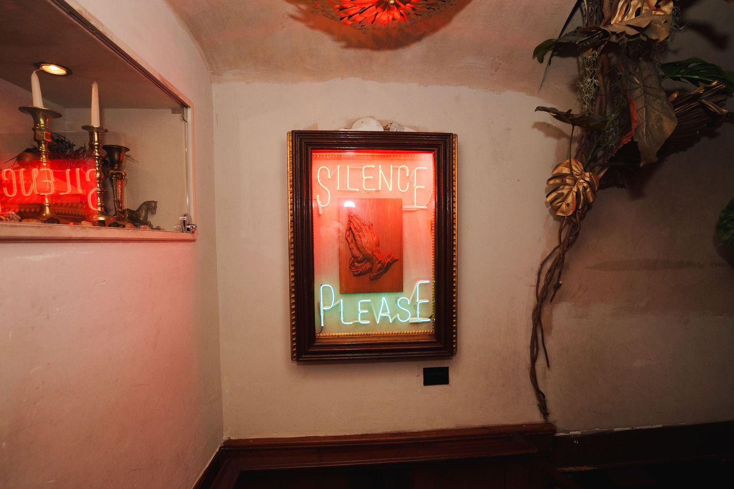 Neon sign reading 'Welcome Please' mounted on a wall with red ambient lighting.