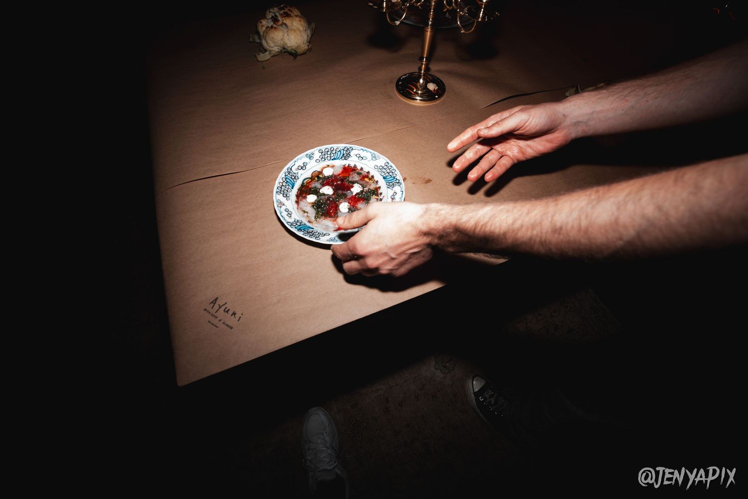 Hands serving appetizers on decorative plates in moody lighting.
