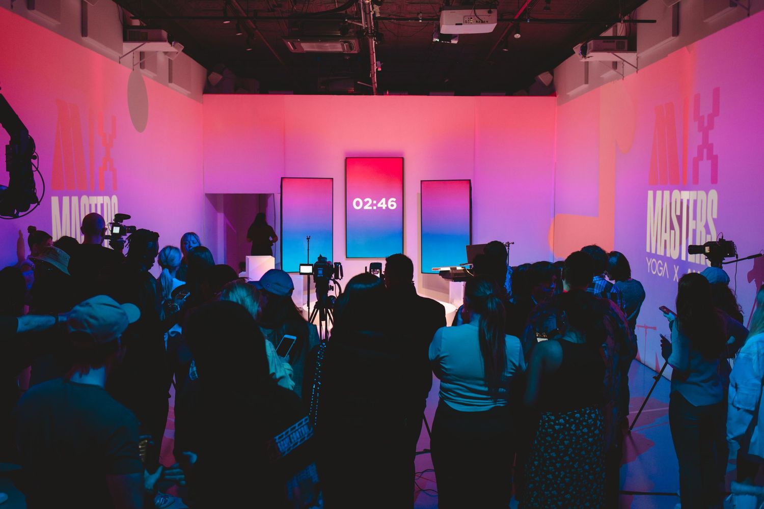 Crowd gathered in studio space with pink ambient lighting and production equipment.