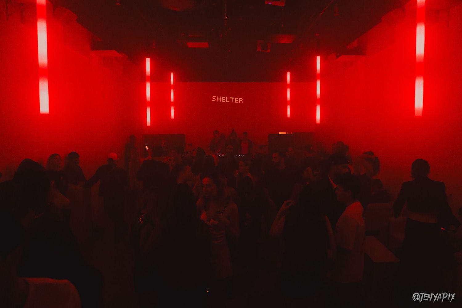 Concert crowd silhouetted in dark venue illuminated by dramatic red lighting and vertical LED strips.