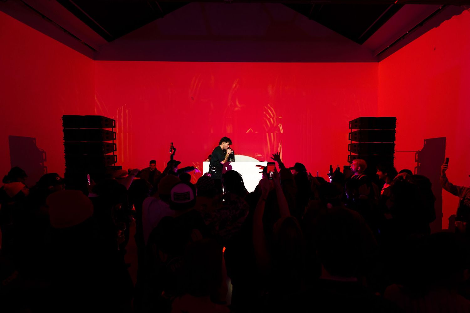 Silhouetted performer and crowd against intense red lighting during concert performance.