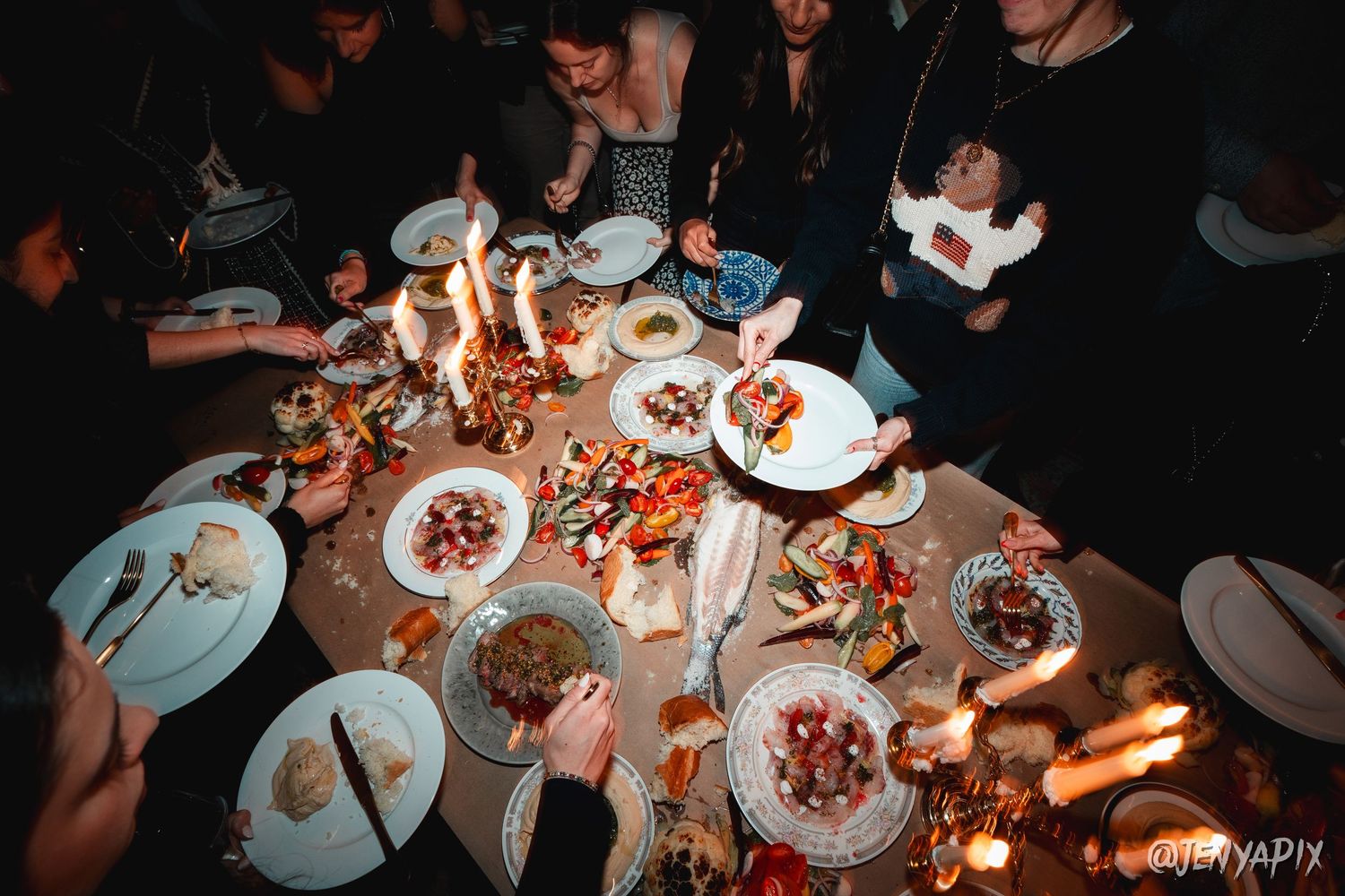 Overhead view of people gathered around a candlelit dinner table with multiple plates.