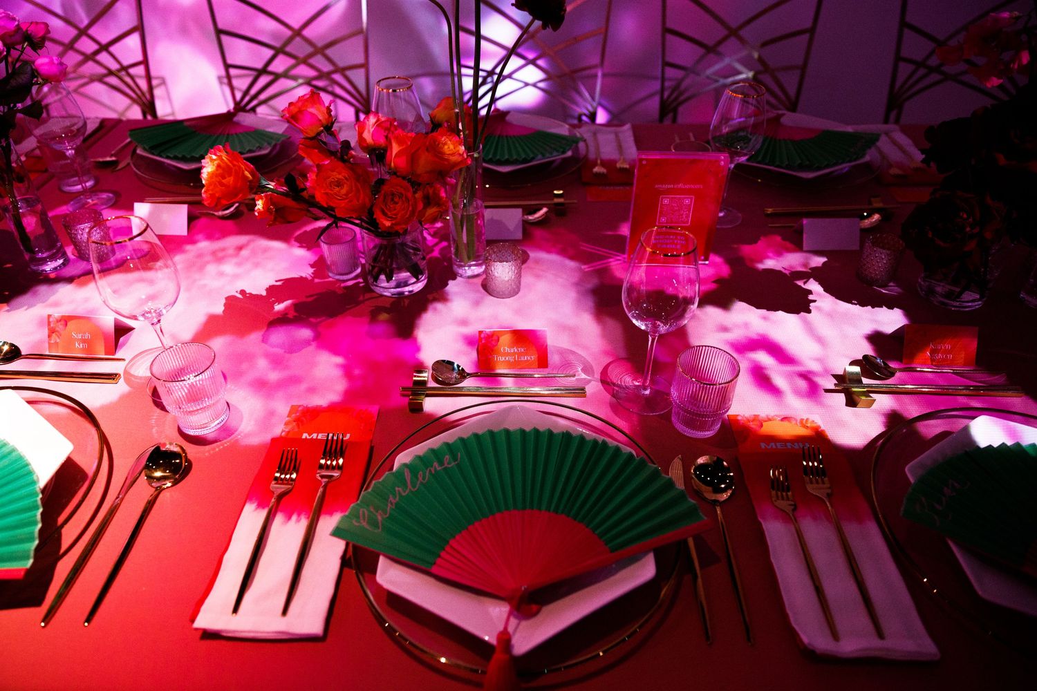 Red and pink themed table decor with ornate fans and floral centerpieces under dramatic lighting.