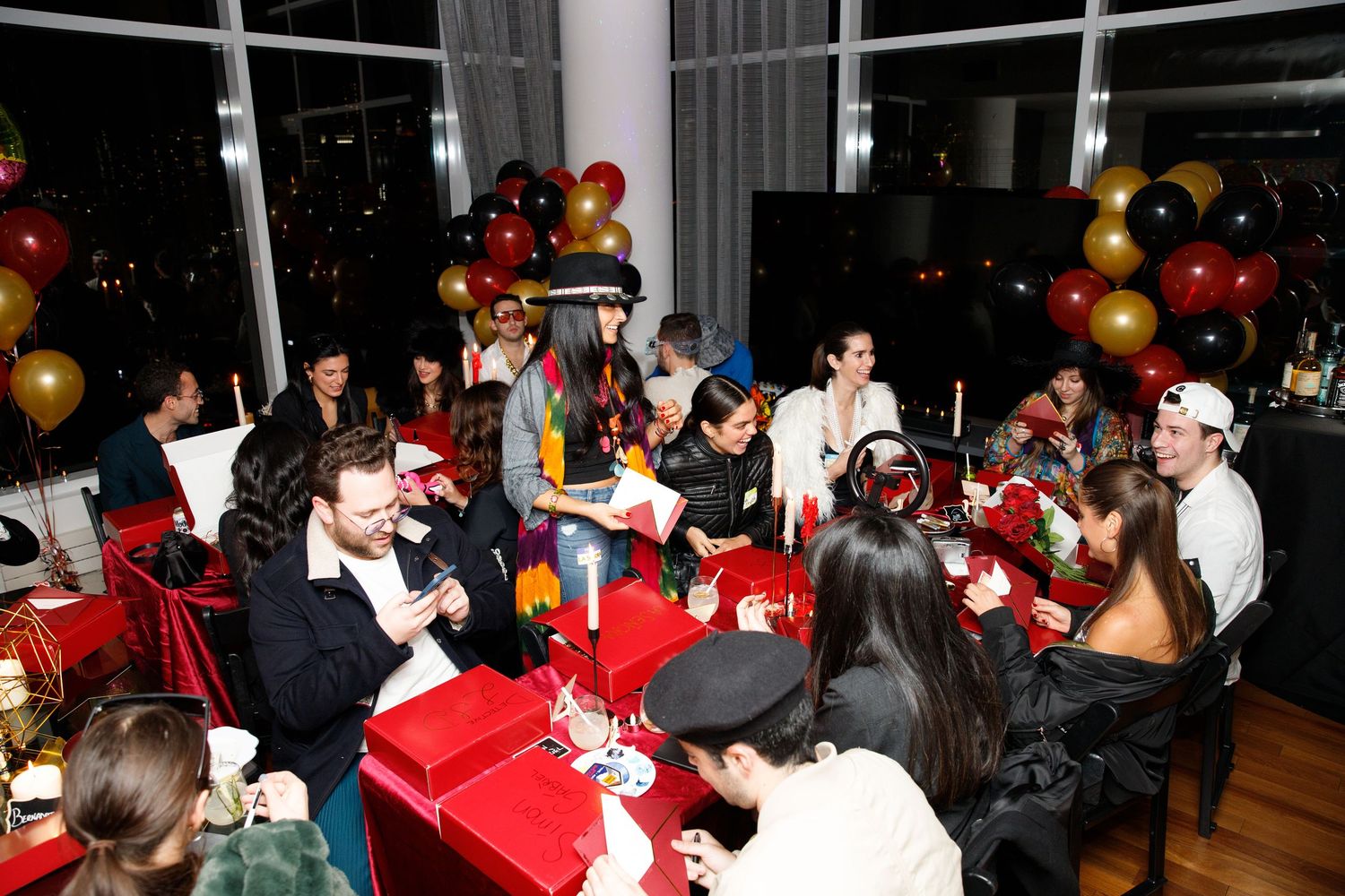 Holiday party scene with guests seated at red-decorated tables and gold balloon arrangements.
