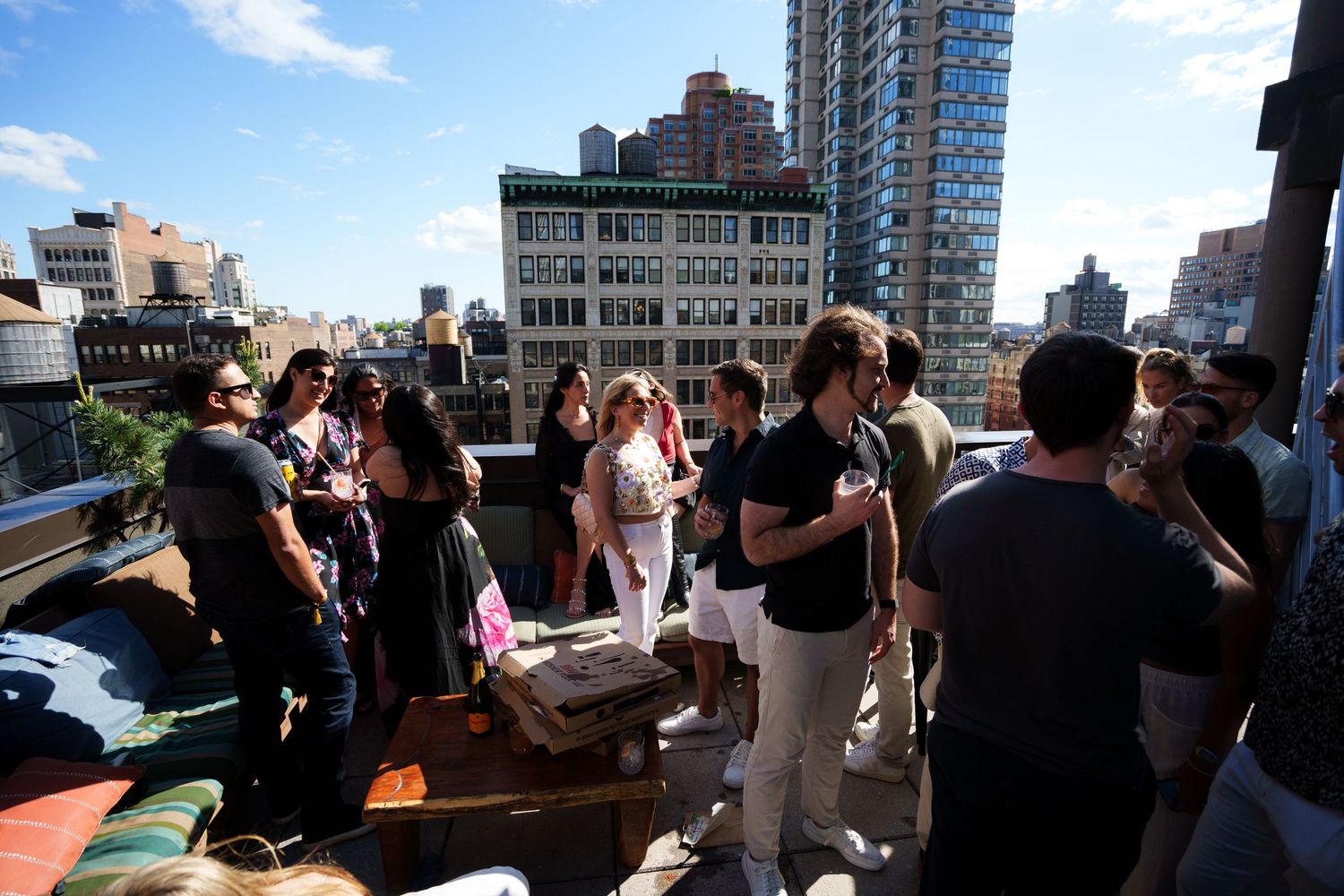 Crowd mingling at daytime rooftop party with urban skyline backdrop.