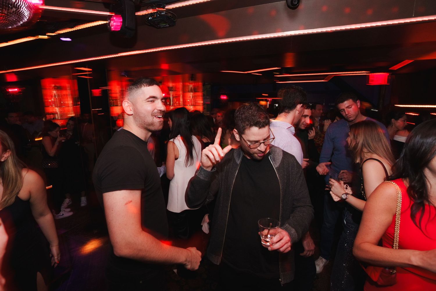Crowded nightclub dance floor with partygoers enjoying music under red lighting.