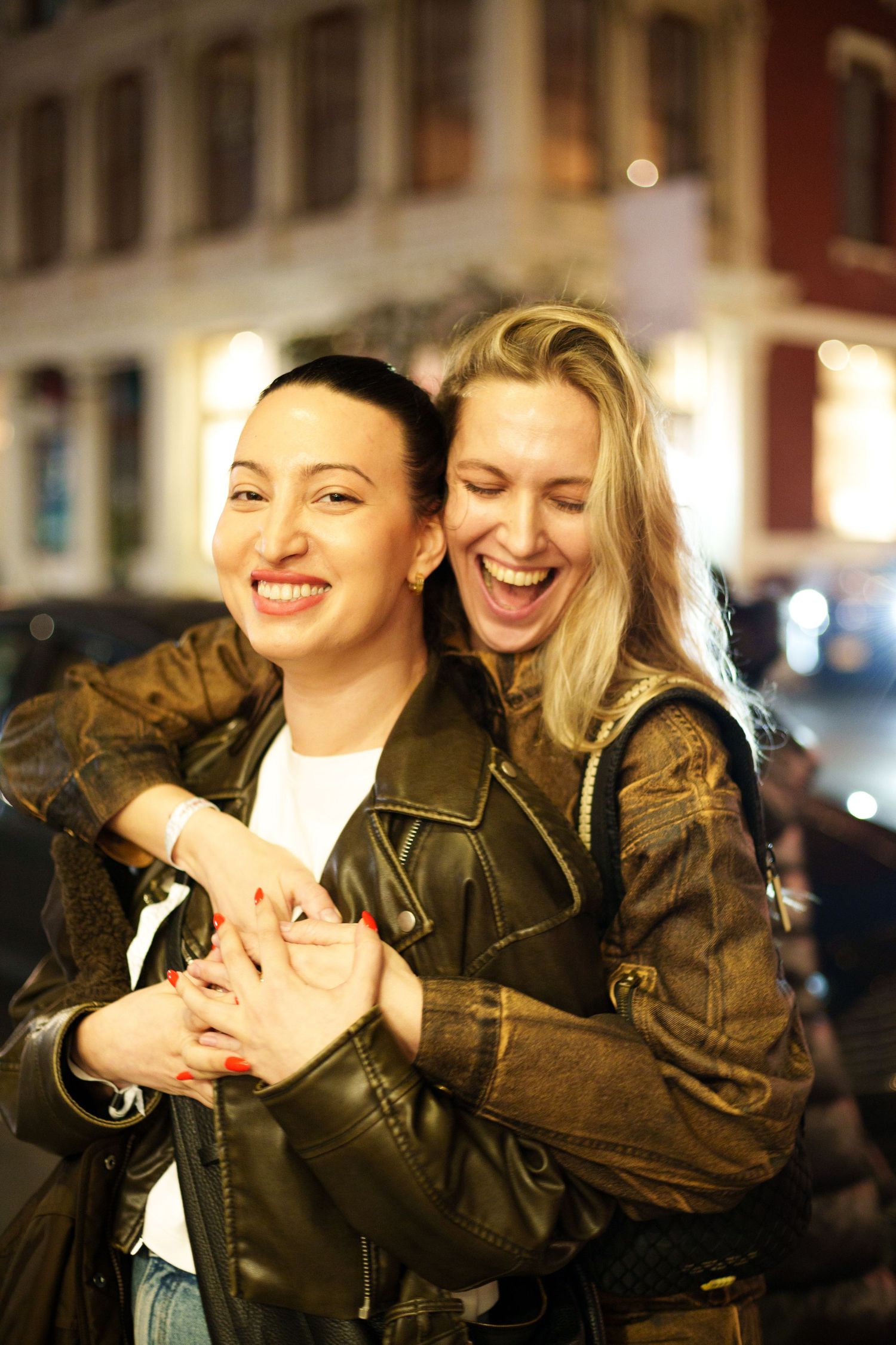 Friends laughing together on nighttime city street wearing matching leather jackets.
