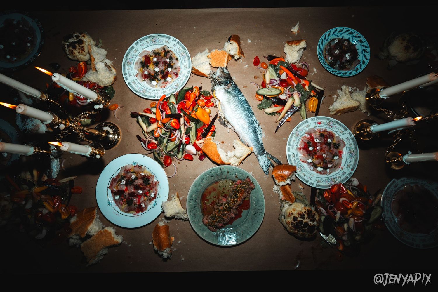 Overhead view of a dinner spread with seafood, plates, and candles on a dark table.