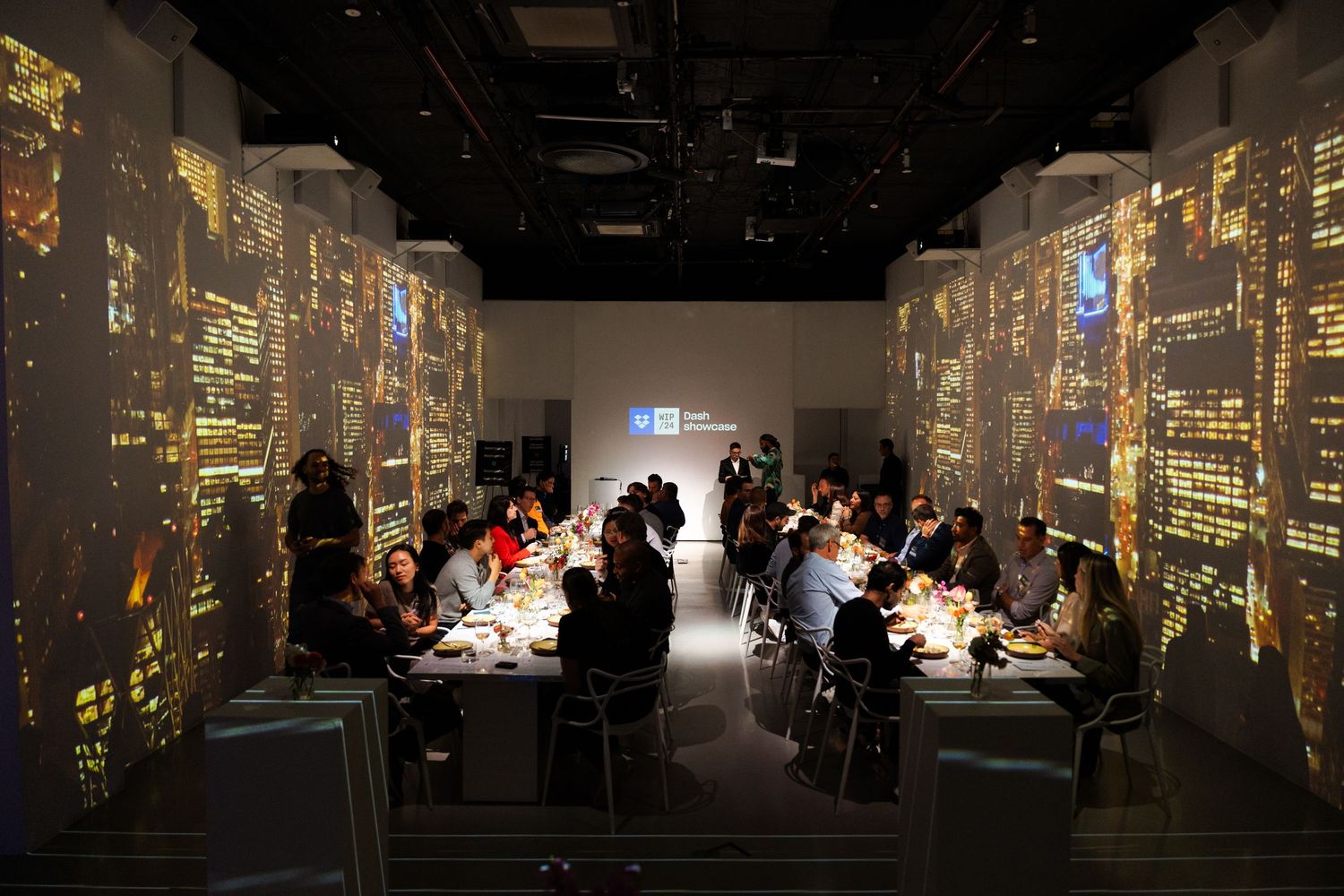 Corporate dinner setting with projected cityscapes on walls creating ambient lighting.