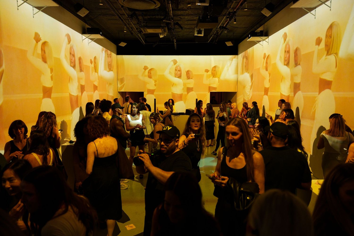 Large gallery exhibition space filled with glowing yellow paper lanterns and attendees viewing the art installation.