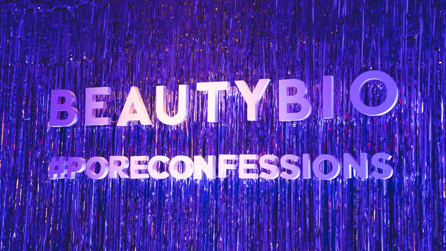 Purple neon sign reading BeautyBio Pore Confessions against sparkly backdrop.