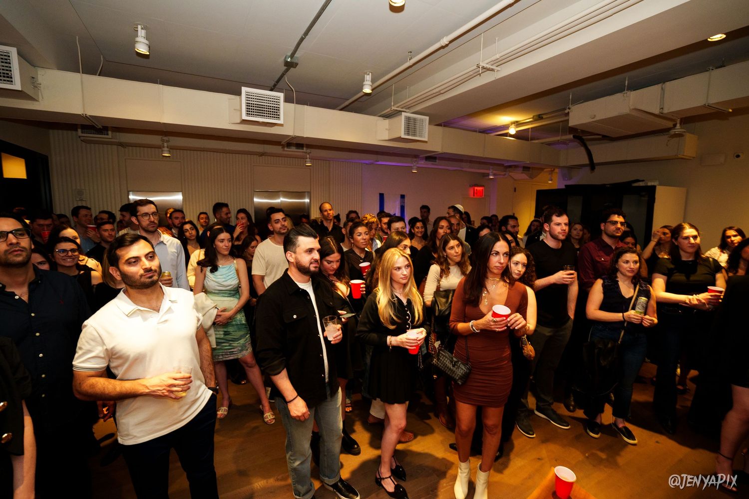 Large crowd of people gathered at an indoor event venue with atmospheric lighting.