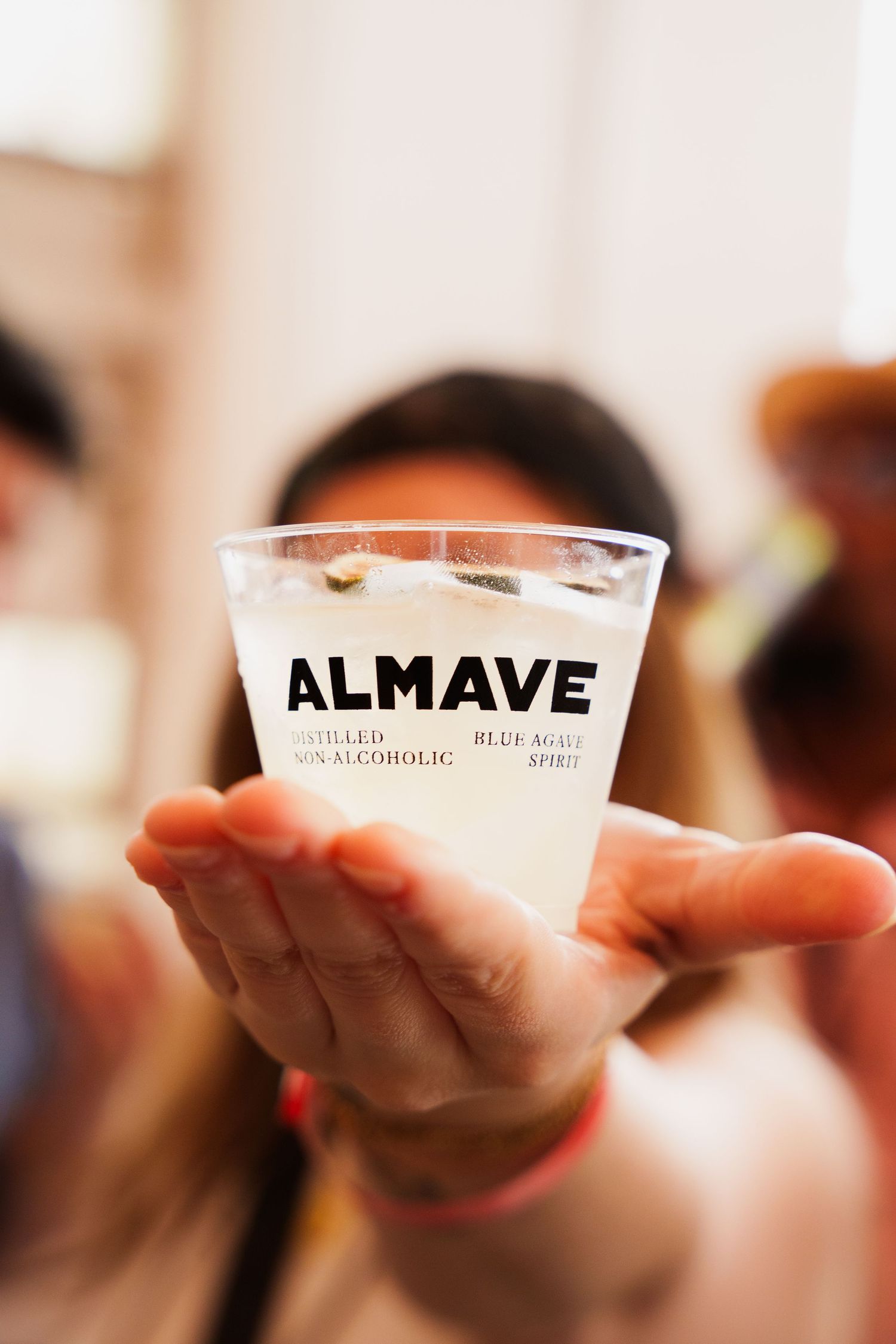 Hand holding up a clear plastic cup with Almave branding.