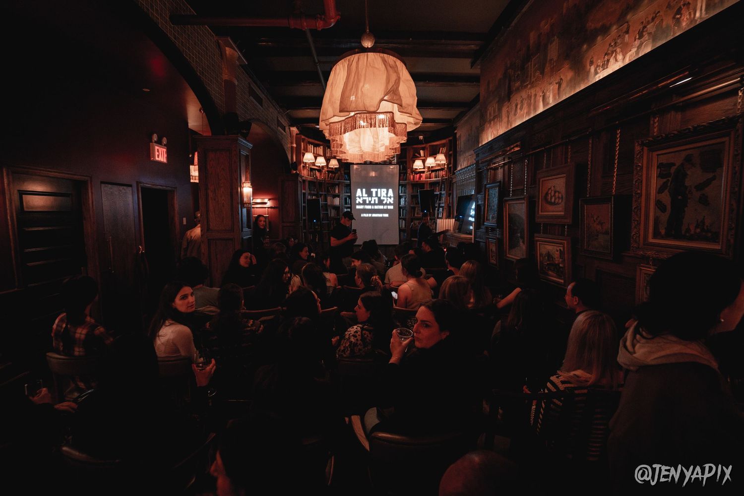 Dimly lit bar interior with crowd gathered under warm pendant lighting.