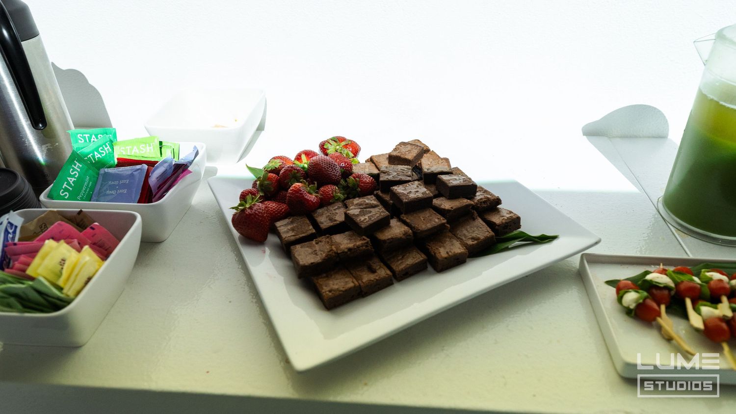 Catering spread featuring chocolate brownies and colorful appetizers on white serving plates.