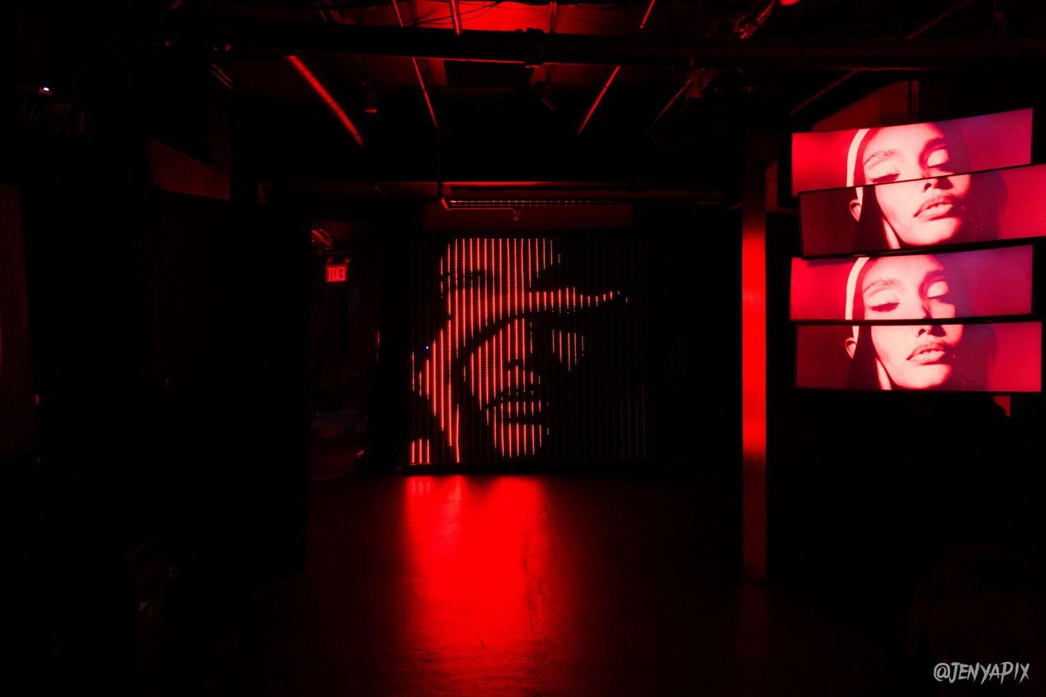 Dark club interior with red lighting and video screen displays showing visual effects.