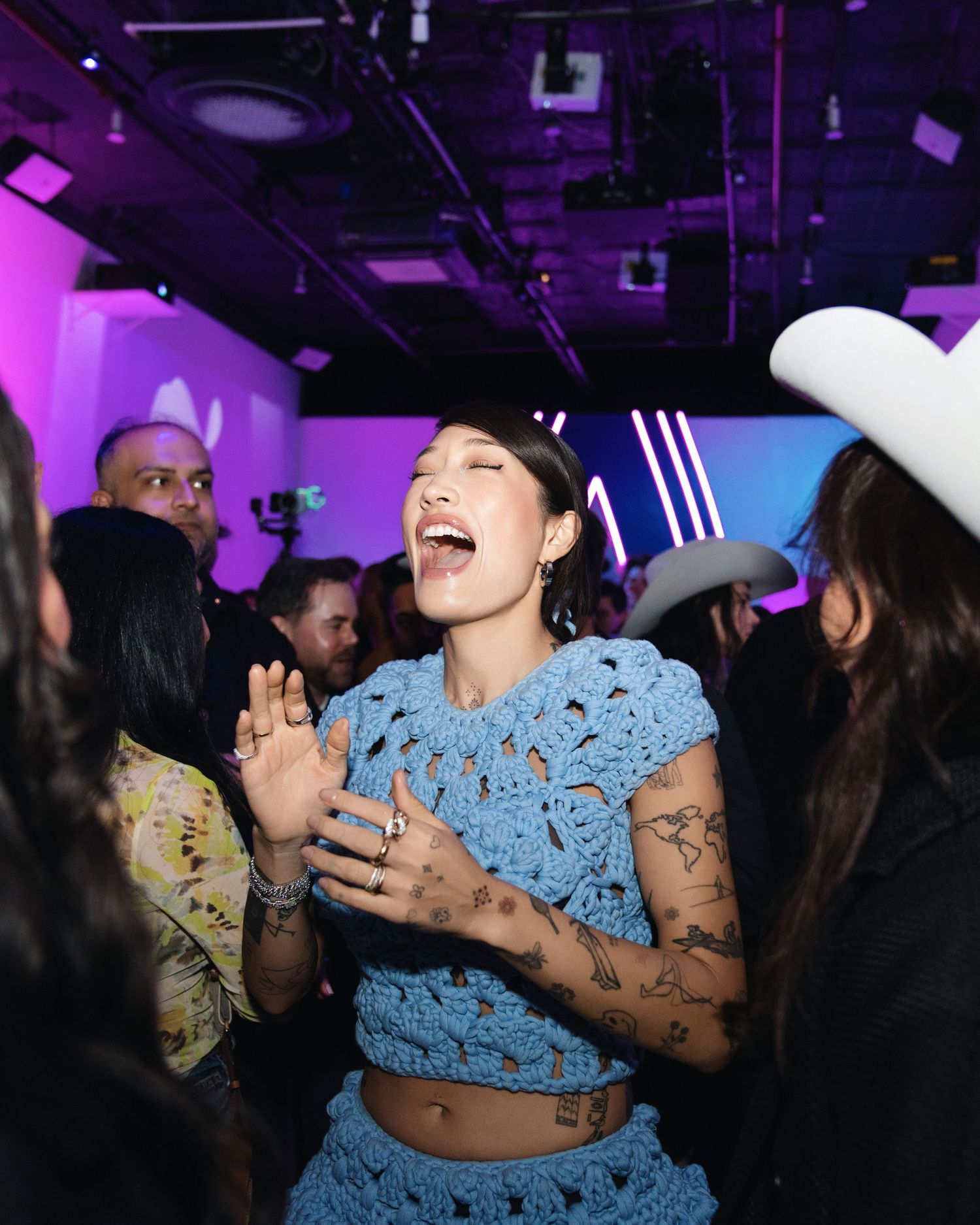 Energetic party scene with person in blue crochet outfit laughing among crowd.