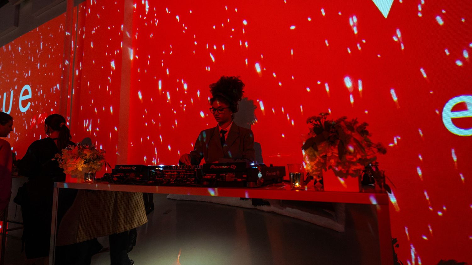 DJ booth setup against dramatic red wall with snow effect projection at Vogue event.