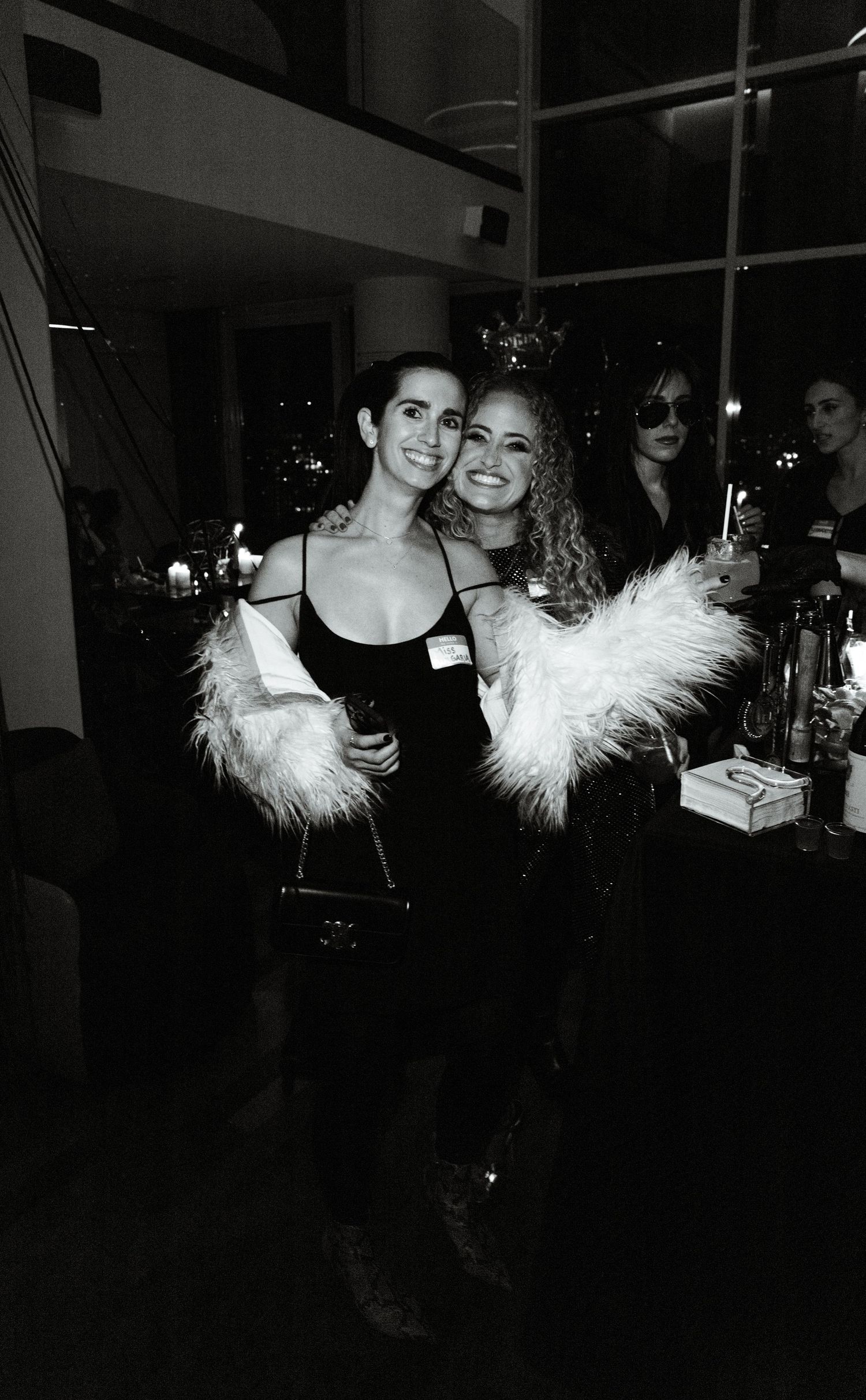 Two friends in stylish outfits with fur accessories enjoy a night out at a party.