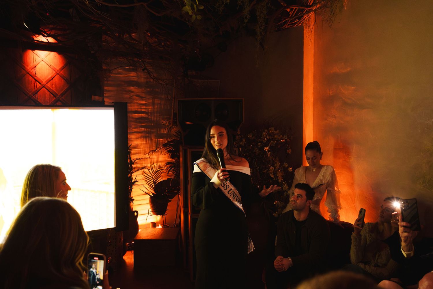 Performance in a dim venue with dramatic orange lighting and projected screen.