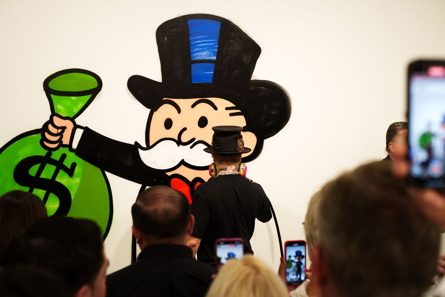 A cartoon character with a top hat and money bag being photographed by audience members.