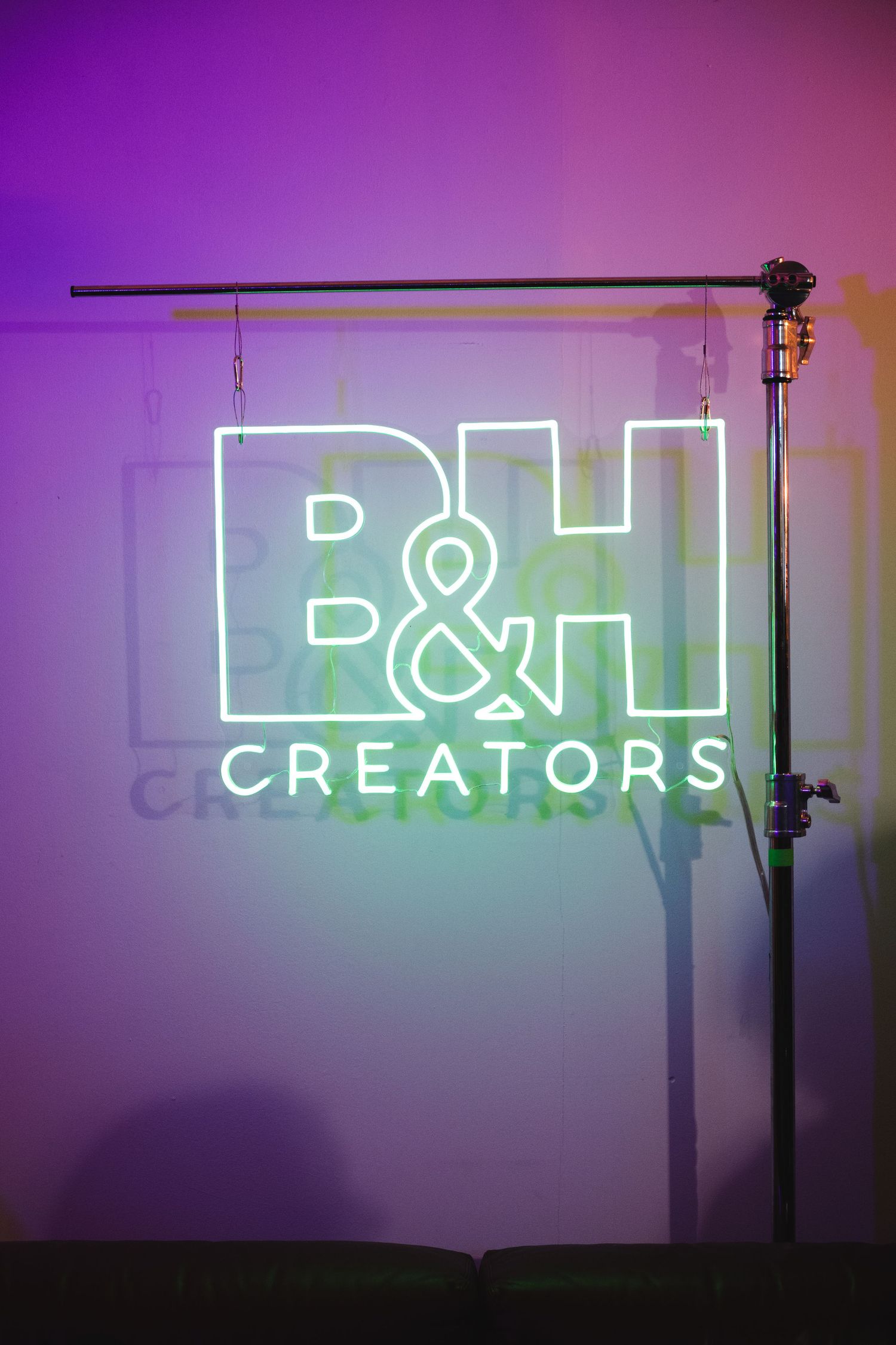 Neon B&H Creators sign glowing against purple-lit wall with lighting equipment.