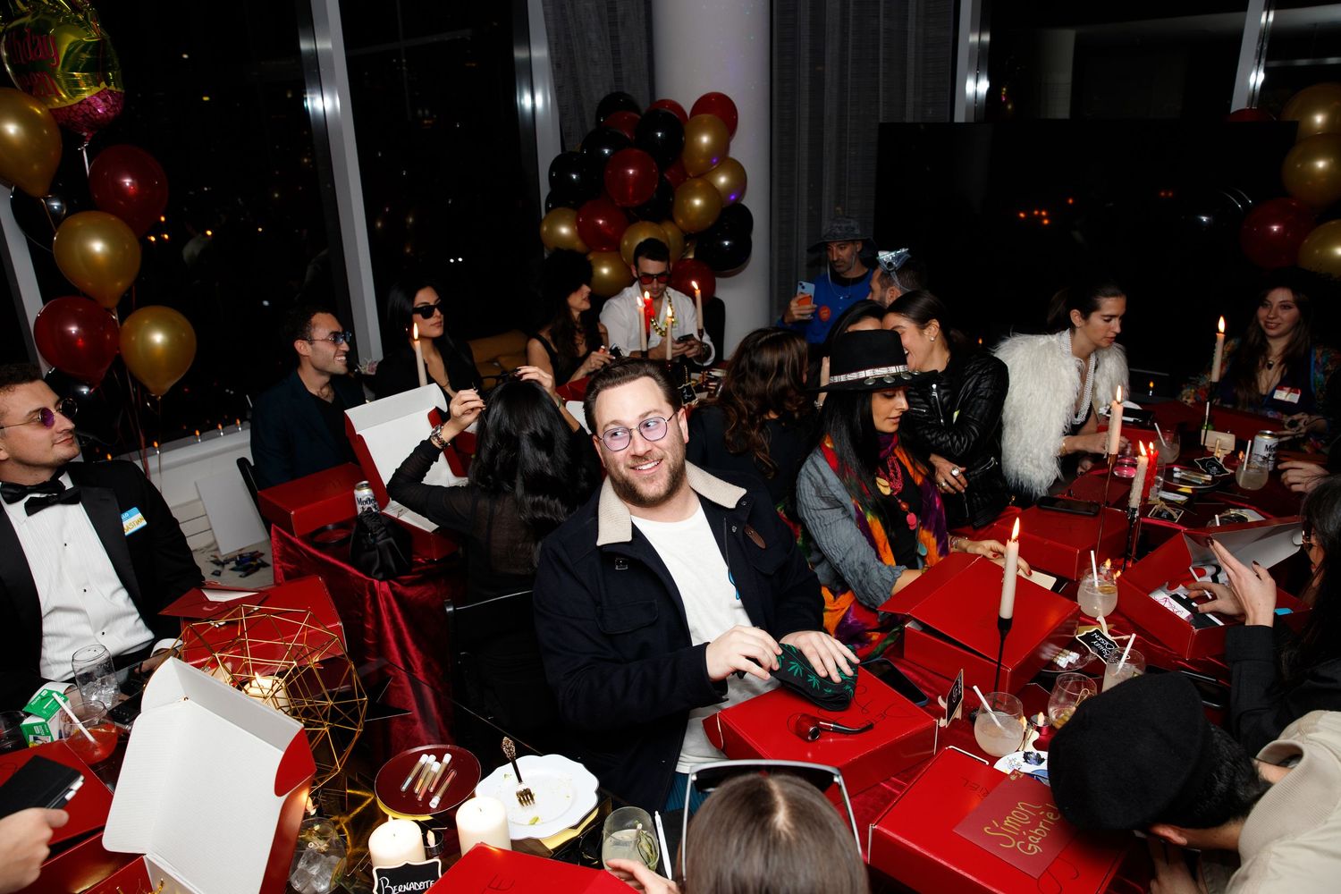 Lively dinner party with guests seated at festive red tables decorated with balloons.