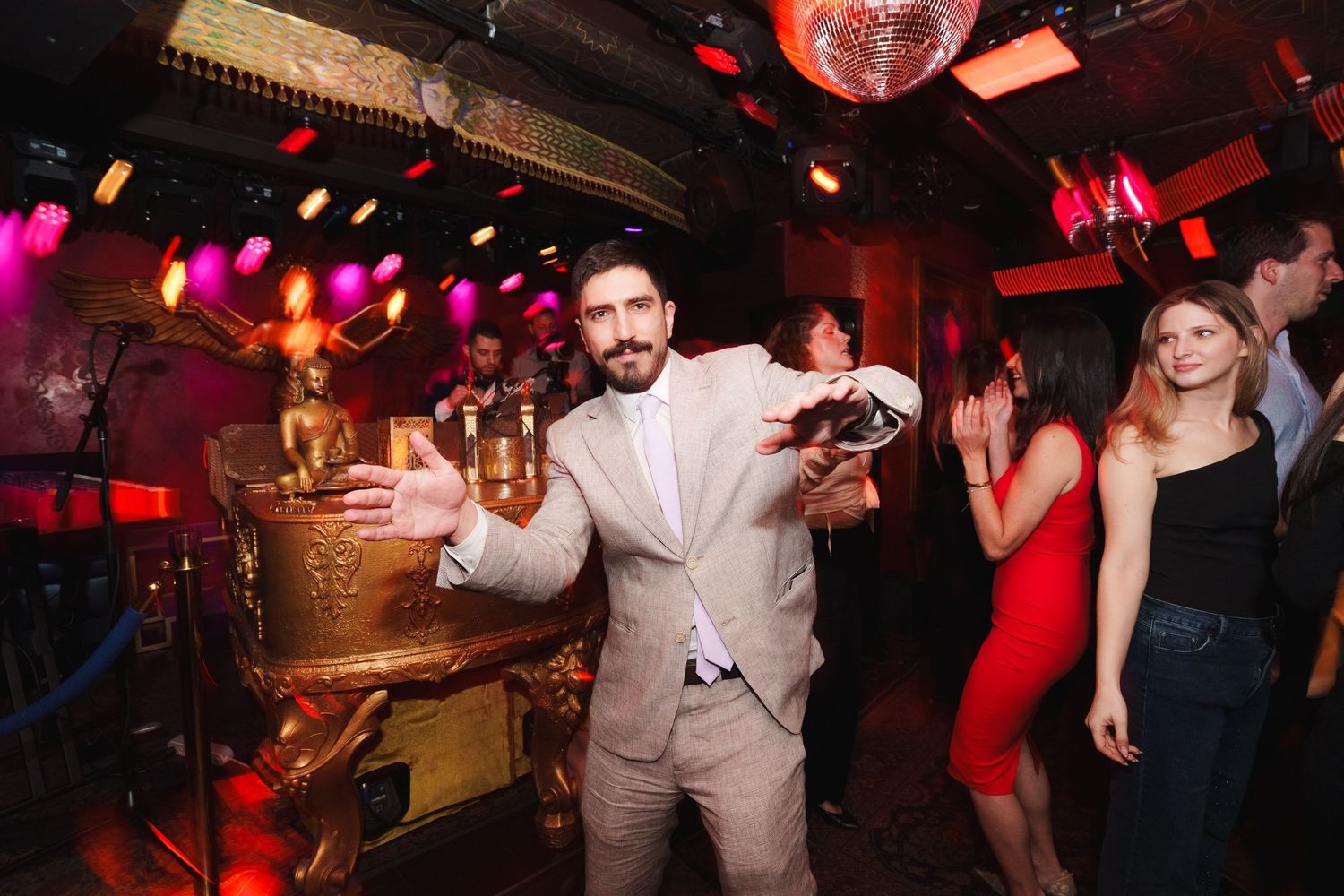 Person in light colored suit celebrating with champagne bottles in nightclub setting.