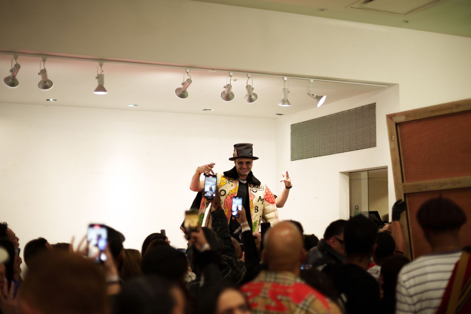 Figure in top hat performing on stage with crowd watching from below.
