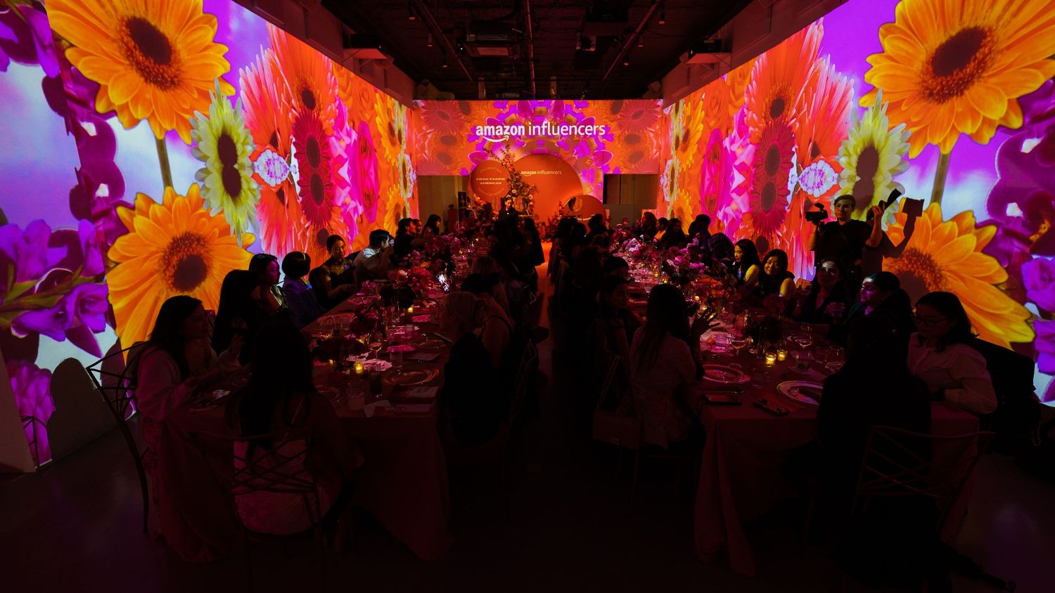 Event space with dramatic pink and orange floral projections illuminating dining tables.
