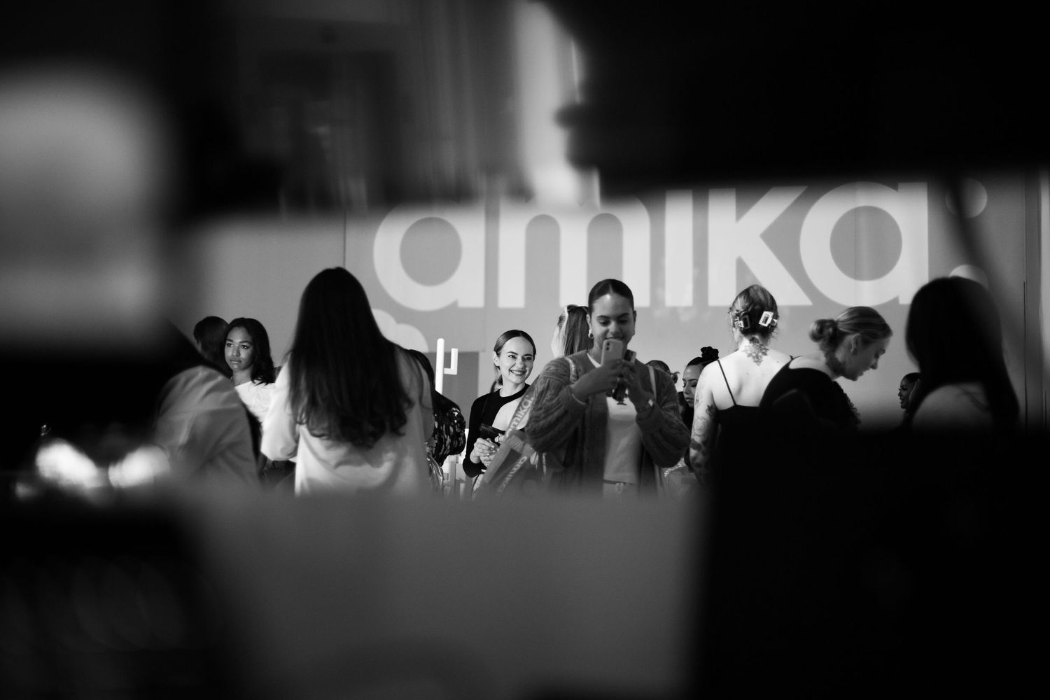 Black and white crowd silhouettes gathered in front of an Amika branded backdrop.