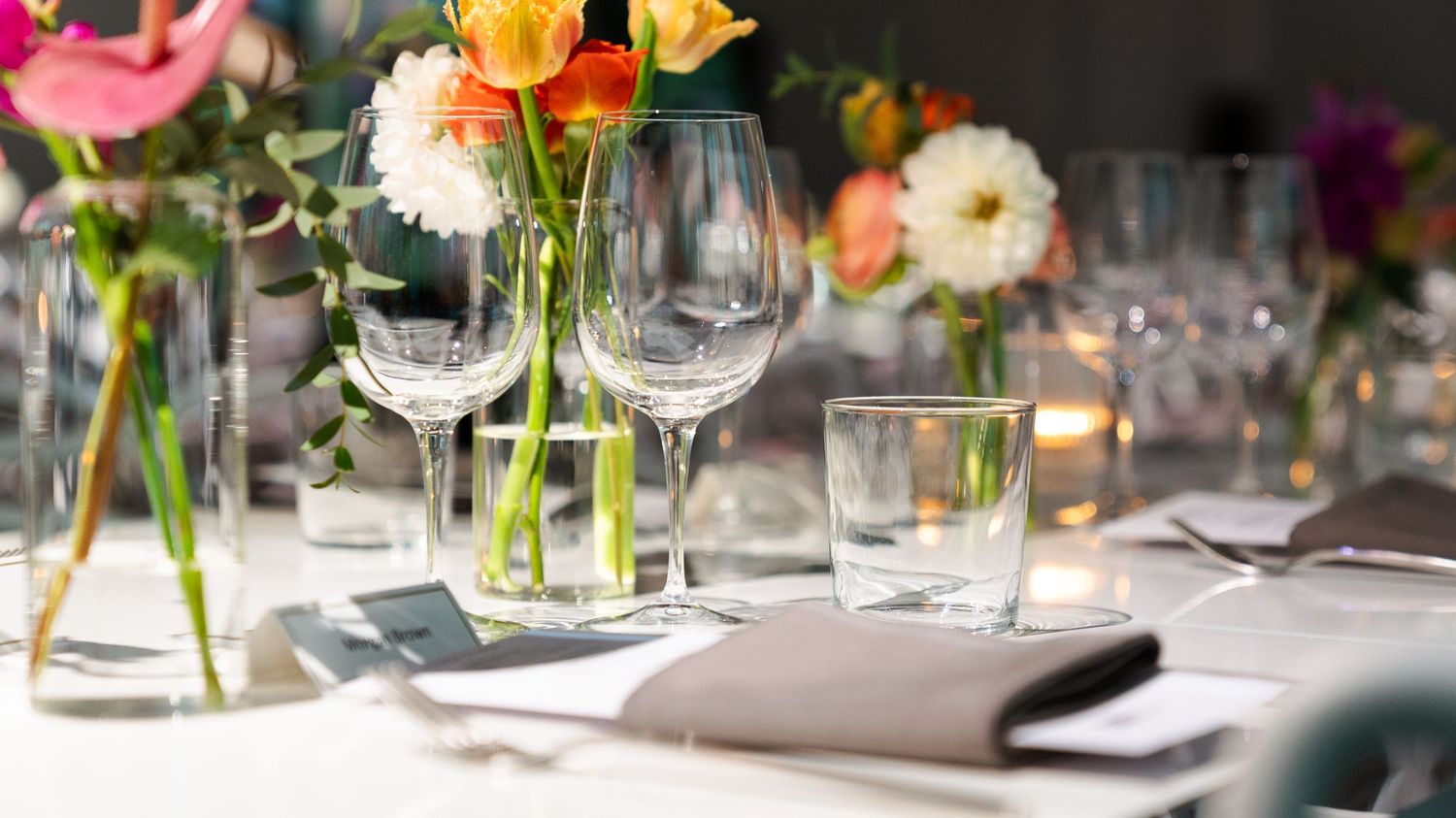 Elegant table setting with colorful flower arrangements and wine glasses in natural light.